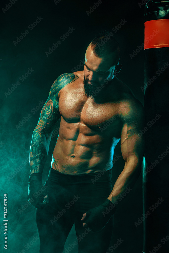 Boxer fighting in gloves with boxing punching bag. Sportsman with tattoos, man Isolated on black background with smoke. Copy Space.