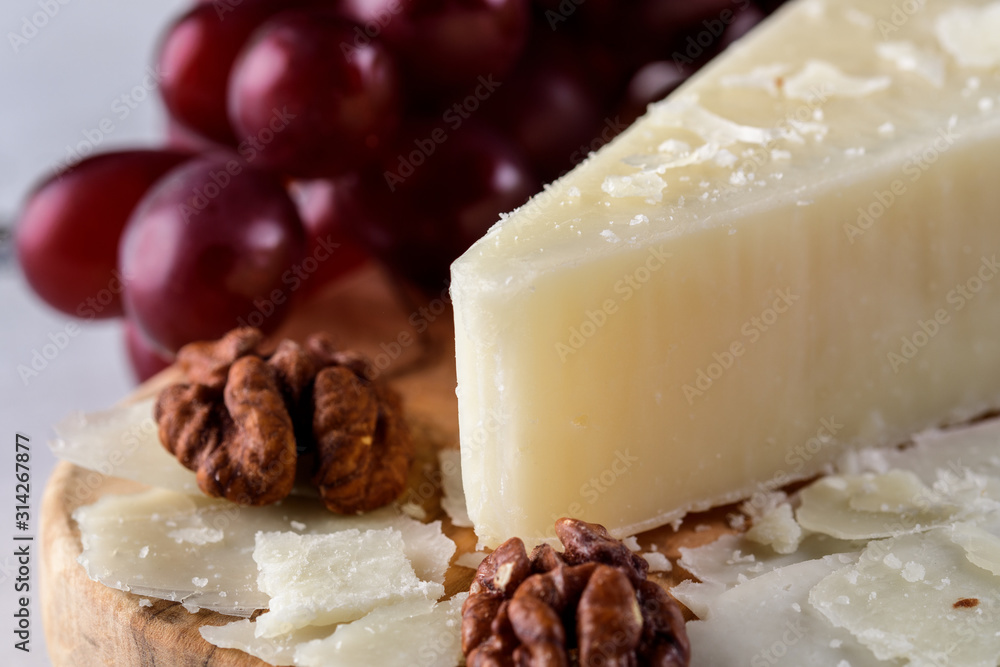 Pecorino romano, hard italian sheep milk cheese on wooden cutting board with grape, selective focus