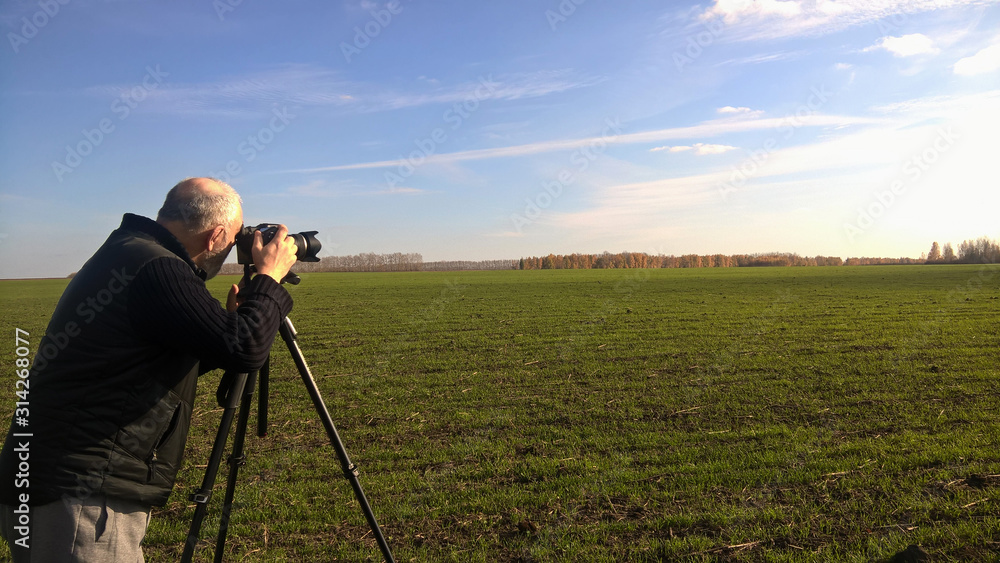 A male photographer in a black jacket takes pictures of a beautiful autumn landscape, clear sky and white clouds. Autumn, Indian summer.