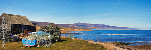 Bild auf Leinwand Old boat, stack of creels and shed at the mouth of the River Brora overlooking t