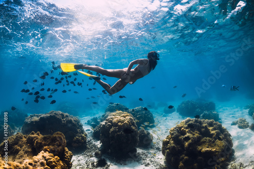 Freediver girl with fins glides over sandy bottom in blue ocean