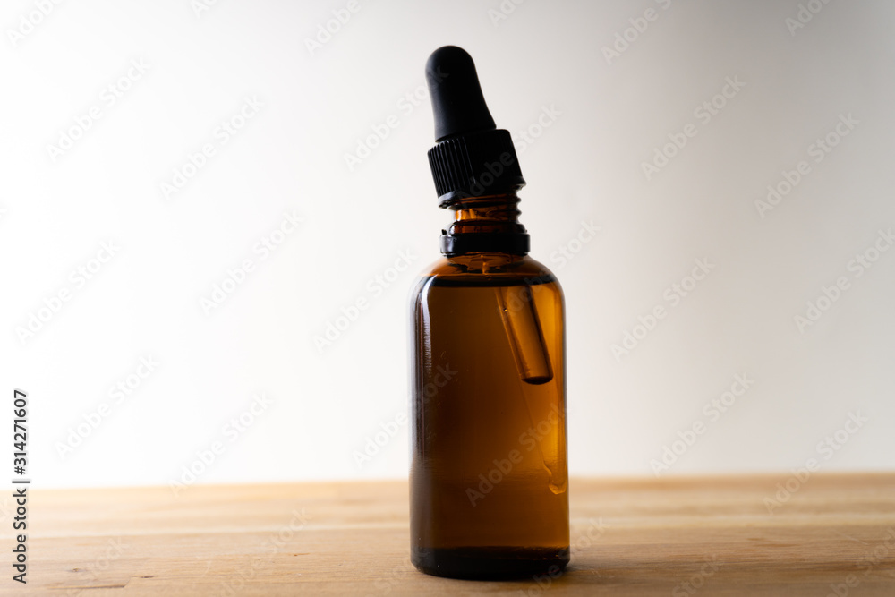 A small bottle with a dropper full of CBD oil or any other oil standing on a wooden board - white background