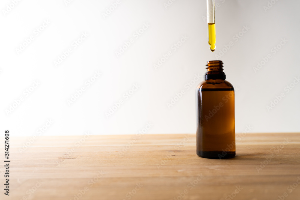 CBD oil or any other oil dropping into a small bottle standing on a wooden board - white background CBD oil or any other oil dropping into a small bottle standing on a wooden board - white background