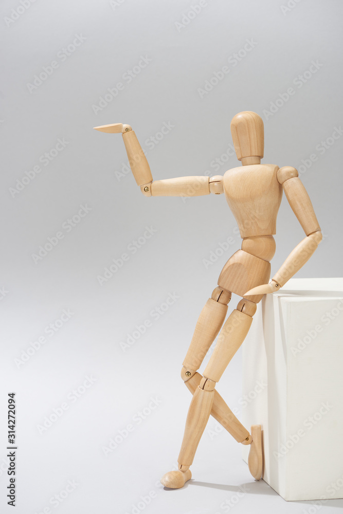 Wooden doll beside white stand point with hand on grey background Wooden doll beside white stand point with hand on grey background