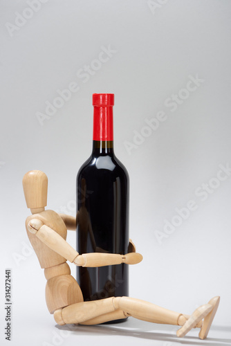 Wooden puppet beside bottle of red wine on grey background