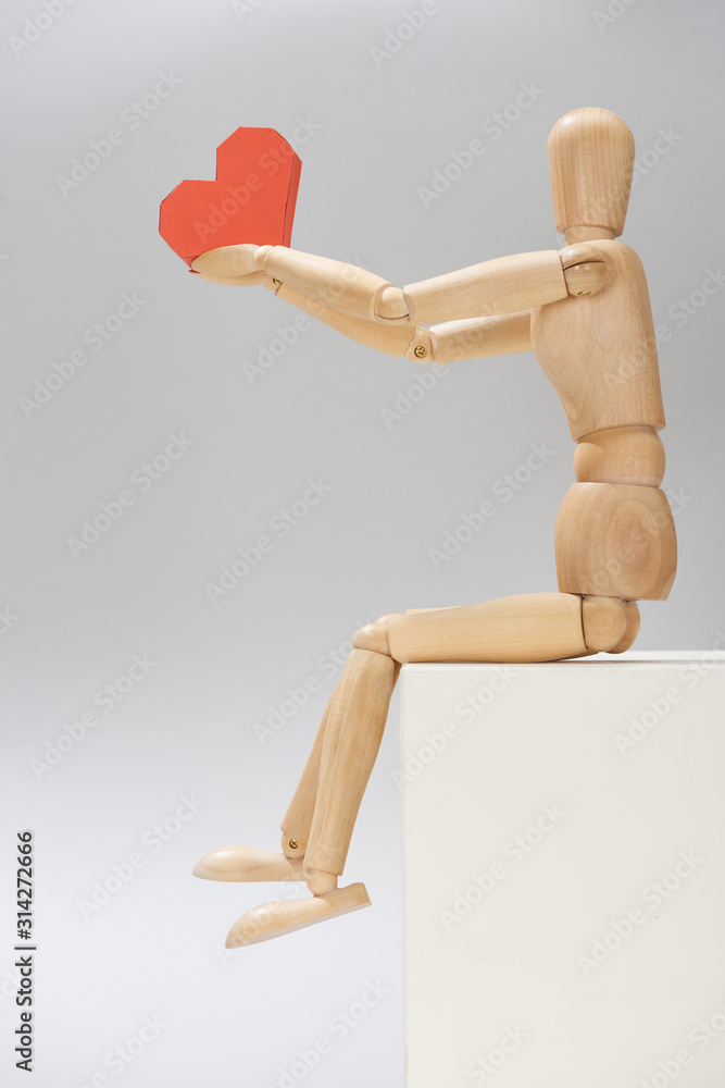 Wooden puppet with paper in heart shape on stand on grey background Wooden puppet with paper in heart shape on stand on grey background