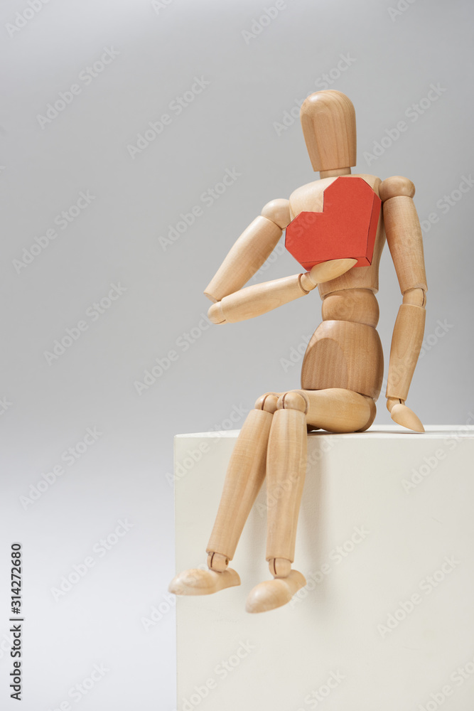 Wooden puppet with red paper heart on stand on grey background Wooden puppet with red paper heart on stand on grey background