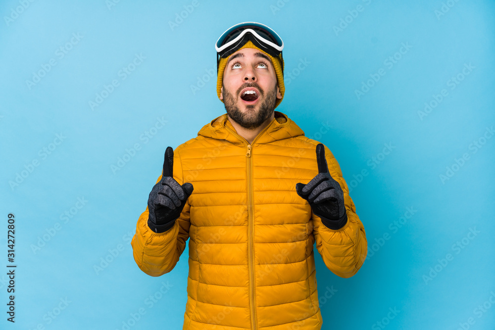Young skier caucasian man isolated pointing upside with opened mouth.
