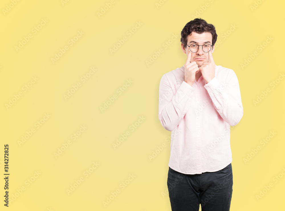 Hesitant young man making a gesture of being careful with his hand pointing at his eye Hesitant young man making a gesture of being careful with his hand pointing at his eye