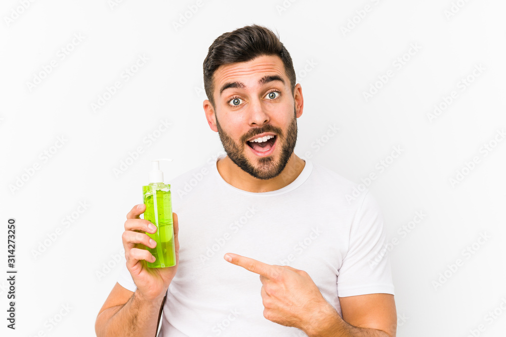 Young caucasian man holding a moisturizer with aloe vera isolated smiling cheerfully pointing with forefinger away. Young caucasian man holding a moisturizer with aloe vera isolated smiling cheerfully pointing with forefinger away.