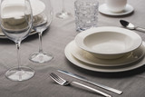Serving dinnerware with cutlery and glasses on grey linen tablecloth