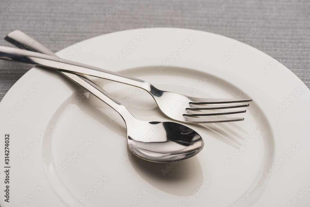 Close up view of shiny spoon and fork on plate on grey surface Close up view of shiny spoon and fork on plate on grey surface