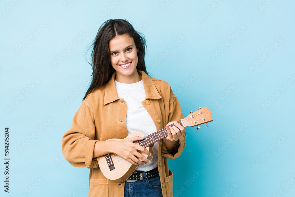 Young caucasian woman playing ukelele isolated on a blue background Young caucasian woman playing ukelele isolated on a blue background