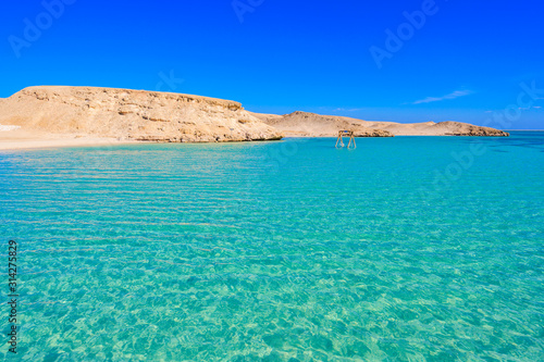 Orange Bay Beach with crystal clear azure water and white beach - hammock in the water for relaxing - paradise coastline of Giftun island, Mahmya, Hurghada, Red Sea, Egypt.