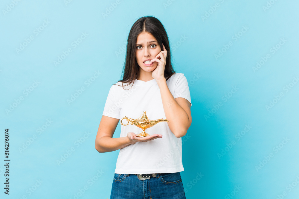 Young caucasian woman holding a magic lamp biting fingernails, nervous and very anxious. Young caucasian woman holding a magic lamp biting fingernails, nervous and very anxious.