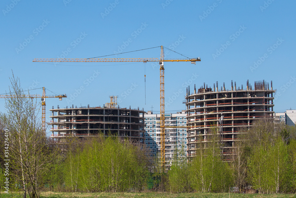 Industrial cranes on a background of high-rise buildings. Modern construction site. Modern industrial urban concept. Tower cranes constructing a new residential building.