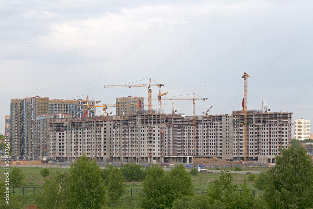 Industrial cranes on a background of high-rise buildings. Modern construction site. Modern industrial urban concept. Tower cranes constructing a new residential building.