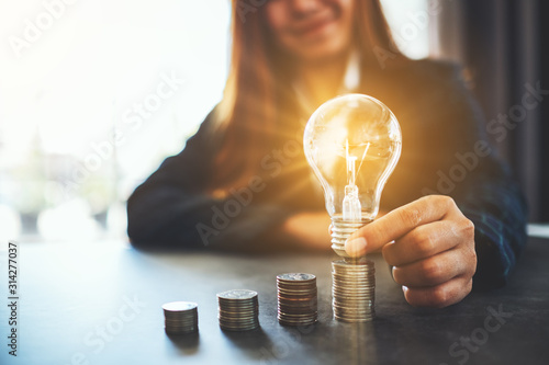 Businesswoman holding and putting lightbulb on coins stack on table for saving energy and money concept photo