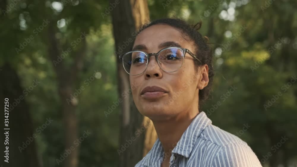 Side view of Pensive pretty african woman in eyeglasses looking away while sitting in the park Side view of Pensive pretty african woman in eyeglasses looking away while sitting in the park