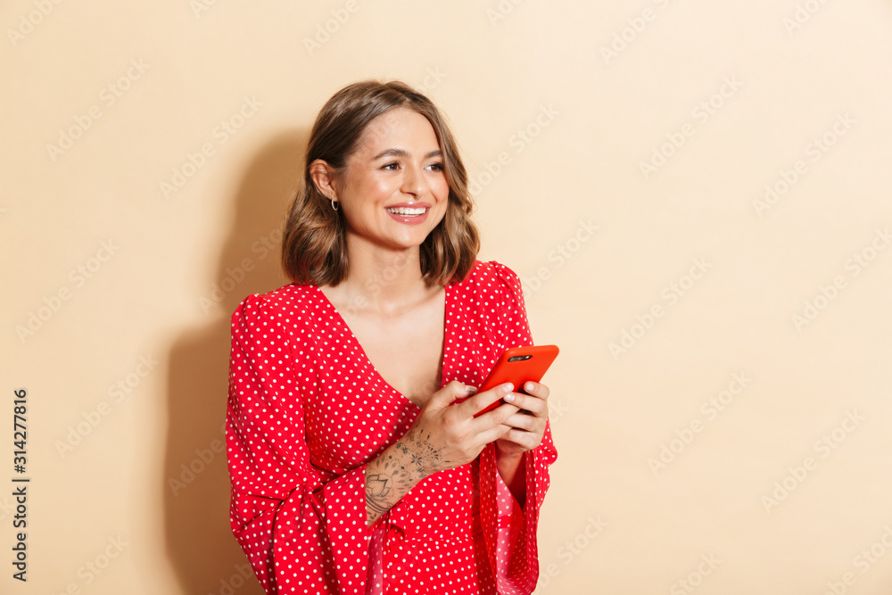 Photo of brunette woman wearing red dress smiling and holding cellphone Photo of brunette woman wearing red dress smiling and holding cellphone