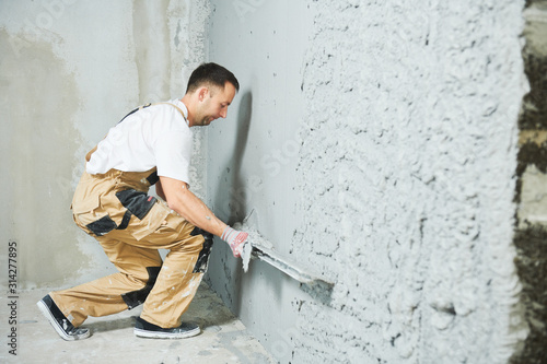 Plasterer using screeder smoothing putty plaster mortar on wall photo