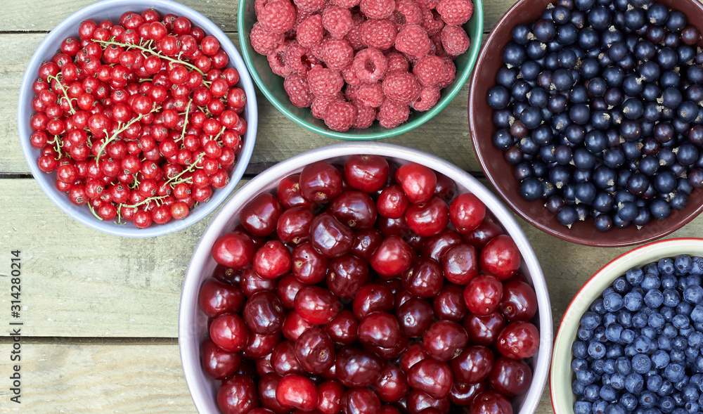 Bowls with fresh garden and forest berries: raspberry, sweet cherries, red and black currant, blueberry, purple shadberry overhead on the wooden table, flat lay, above top view, closeup, empty space Bowls with fresh garden and forest berries: raspberry, sweet cherries, red and black currant, blueberry, purple shadberry overhead on the wooden table, flat lay, above top view, closeup, empty space