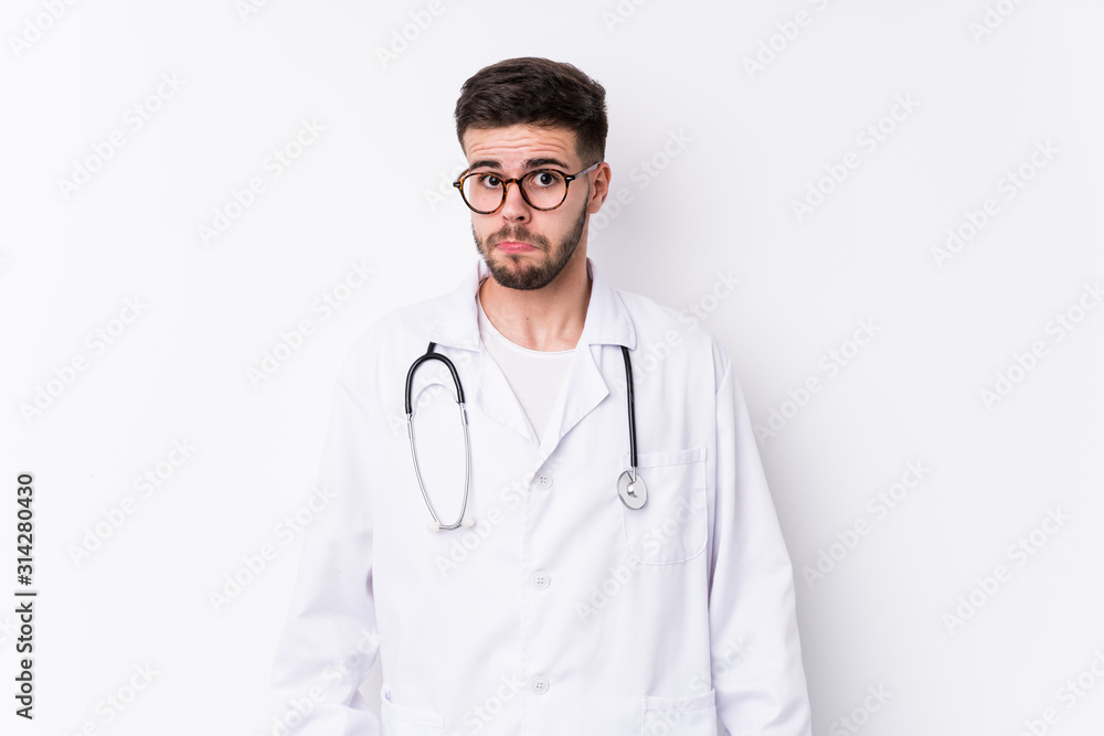 Young caucasian doctor man isolated shrugs shoulders and open eyes confused. Young caucasian doctor man isolated shrugs shoulders and open eyes confused.