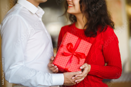 Man gives to his woman a gift box with red ribbon. A loving couple cuddles and celebrating Valentine's Day in the restaurant. Valentine's Day, holiday and surprise concept. Relationship and love. © maxbelchenko