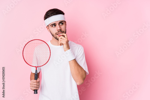 Young caucasian man playing badminton isolated relaxed thinking about something looking at a copy space. © Asier