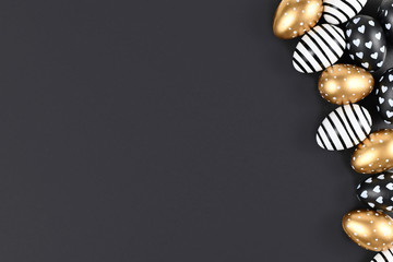 Flat lay with golden, black and white easter eggs painted with stripes, hearts and dots on black background with blank copy space
