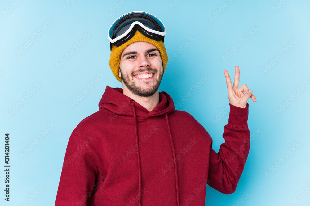 Young caucasian man wearing a ski clothes isolated joyful and carefree showing a peace symbol with fingers. Young caucasian man wearing a ski clothes isolated joyful and carefree showing a peace symbol with fingers.