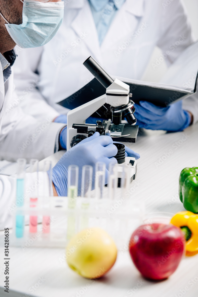selective focus of molecular nutritionist using microscope and colleague holding folder on background selective focus of molecular nutritionist using microscope and colleague holding folder on background