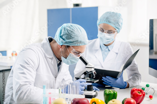 molecular nutritionist holding folder and looking at colleague with microscope