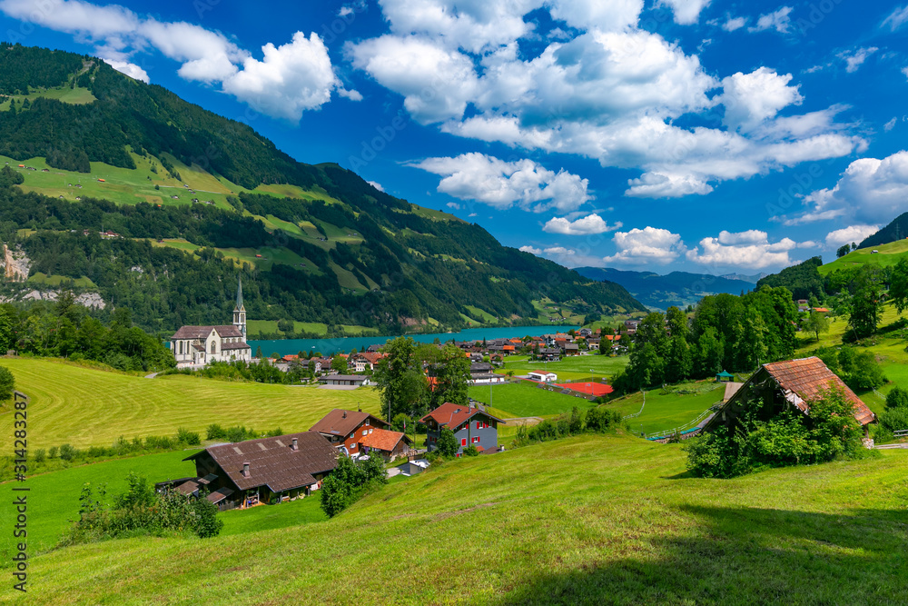 Catholic church, traditional wood and modern houses along the lake Lungernsee in swiss village Lungern in sunny summer day, Obwalden, Switzerland