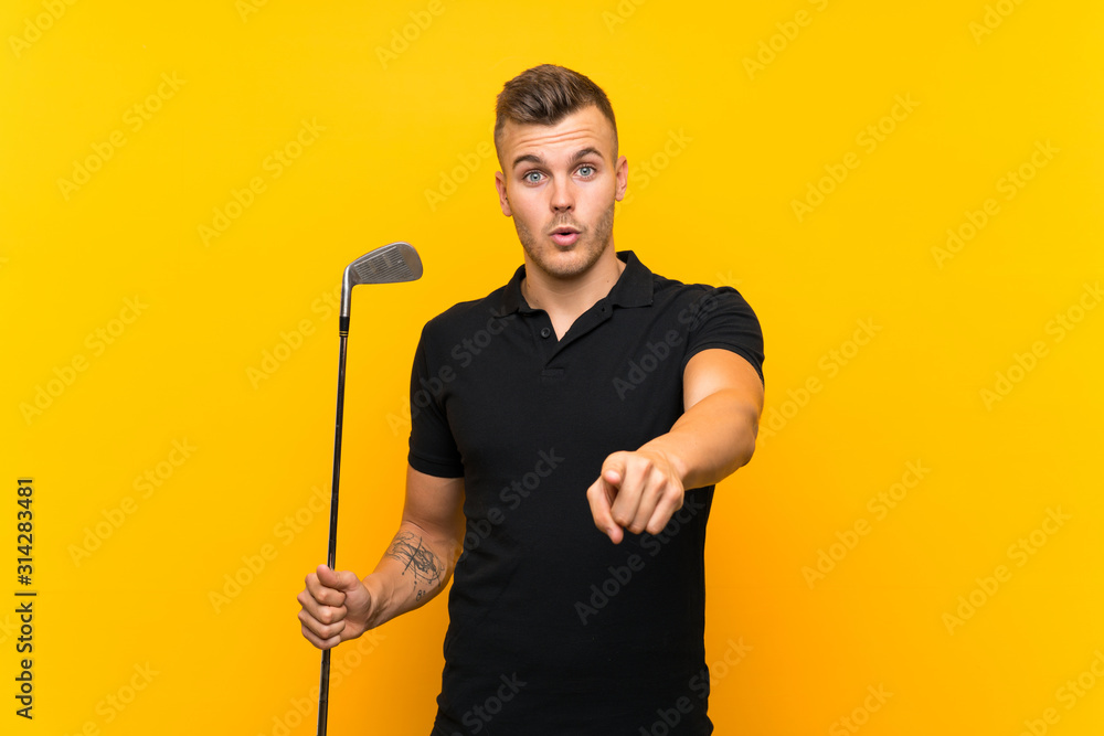 Golfer player man over isolated yellow background surprised and pointing front Golfer player man over isolated yellow background surprised and pointing front