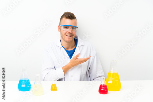 Young scientific with lots of laboratory flask extending hands to the side for inviting to come