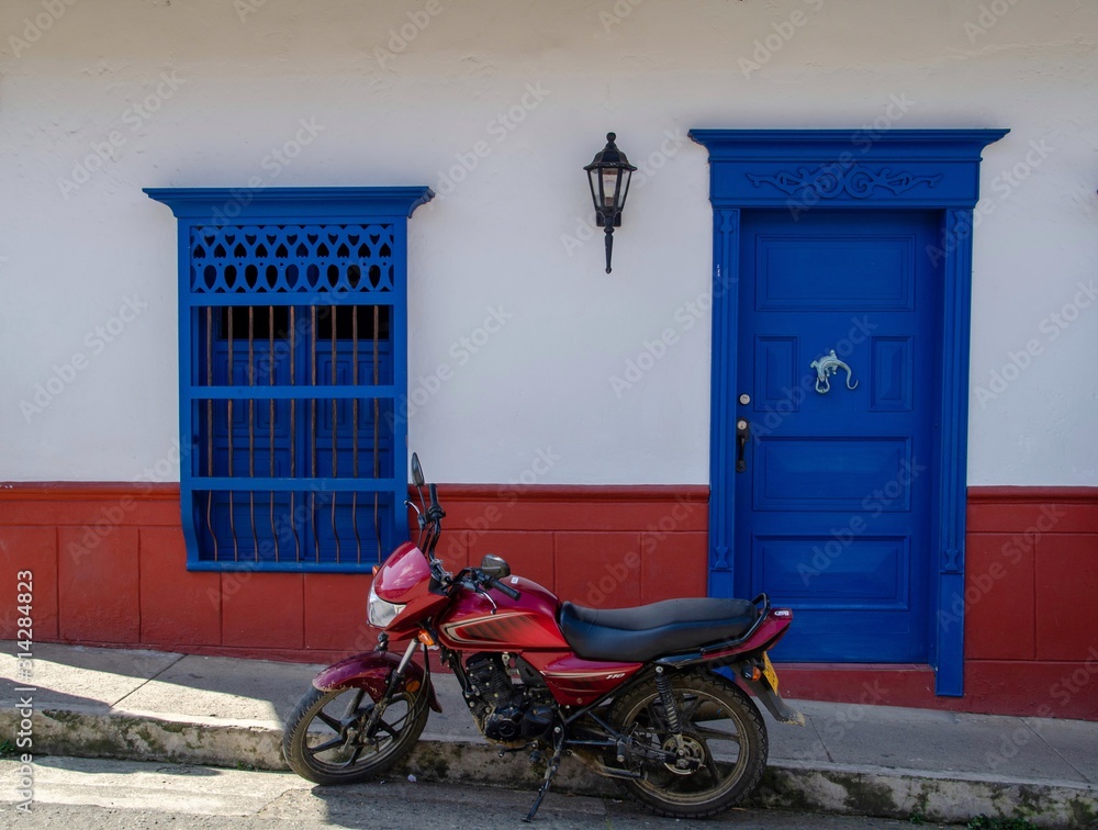 Puerta y ventana en madera azul con zocalo rojo sobre fachada blanca
