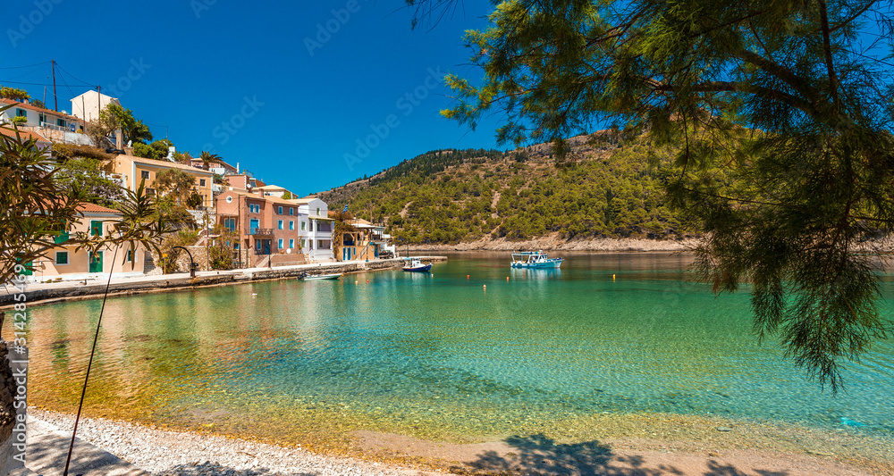 Amazing coastline with colorful houses under sunlight. Wonderful summer seascape with perfect blue sky of Ionian Sea. Assos village. Kefalonia. Greece