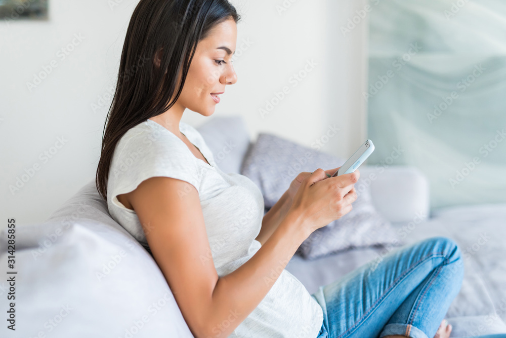 Smiling young woman reading sms while sitting on couch Smiling young woman reading sms while sitting on couch