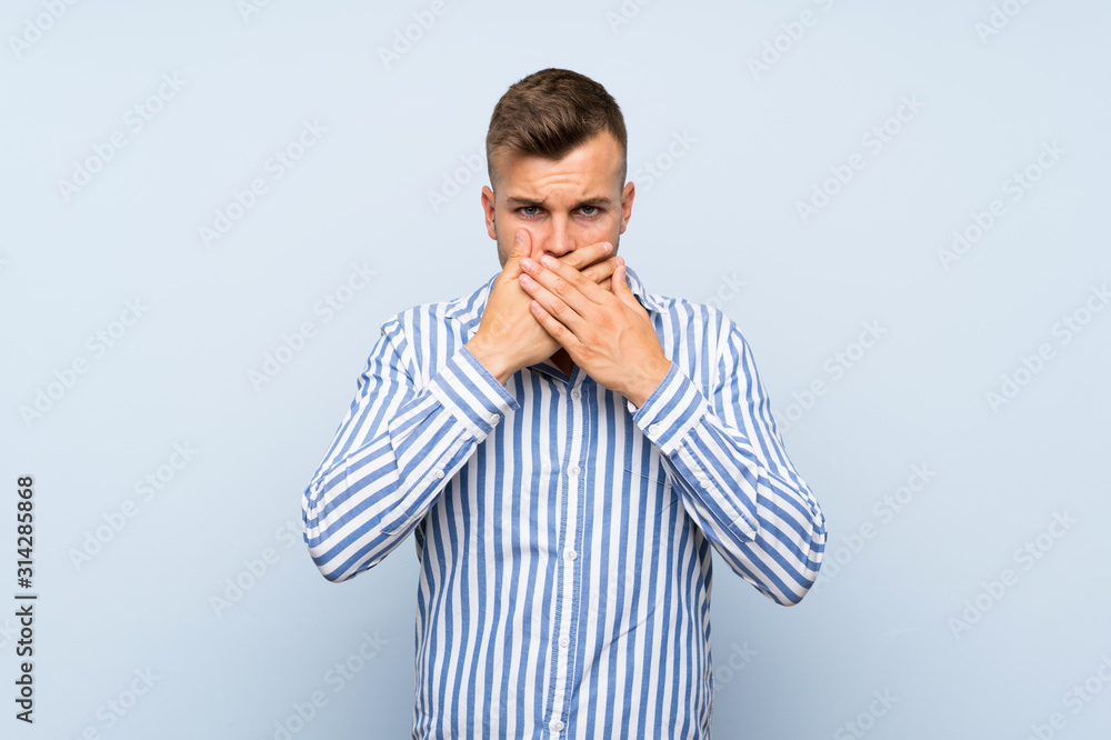 Young handsome blonde man over isolated blue background covering mouth with hands Young handsome blonde man over isolated blue background covering mouth with hands