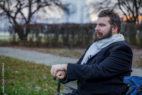 Middle adult bearded man have rest with closed eyed and smiling face on bench in autumn park hold umbrella cane