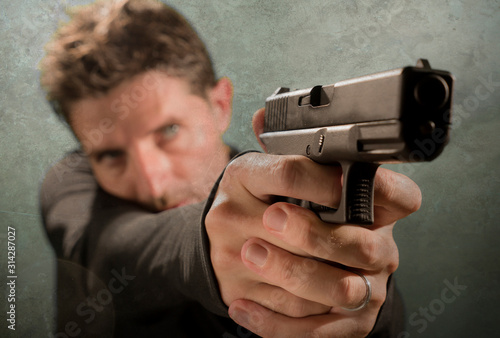 grunge cinematic portrait of attractive and dangerous looking hitman or secret service especial agent man in action pointing gun in crime mob and criminal lifestyle concept photo