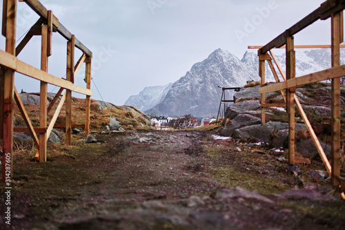 Cod fish drying wood constructions with village and snowy mountain horizon. Henningsvaer, Lofoten Norway.