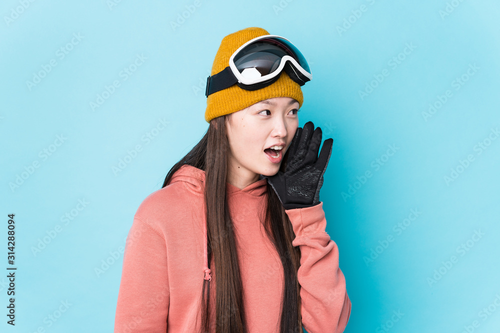 Young chinese woman wearing ski clothes isolated shouting and holding palm near opened mouth. Young chinese woman wearing ski clothes isolated shouting and holding palm near opened mouth.
