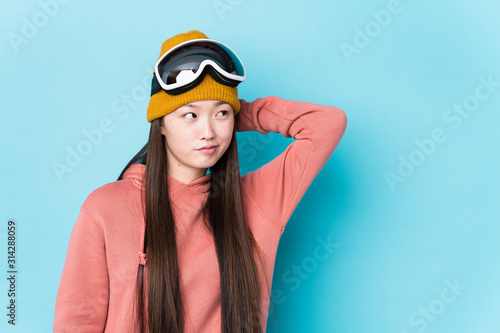 Young chinese woman wearing ski clothes isolated touching back of head, thinking and making a choice. © Asier