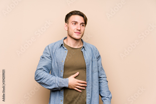 Young caucasian man posing isolated touches tummy, smiles gently, eating and satisfaction concept.