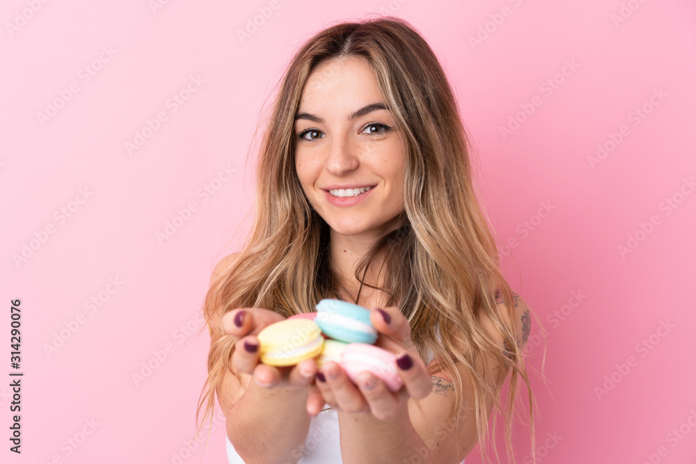 Young woman over isolated pink background holding colorful French macarons Young woman over isolated pink background holding colorful French macarons