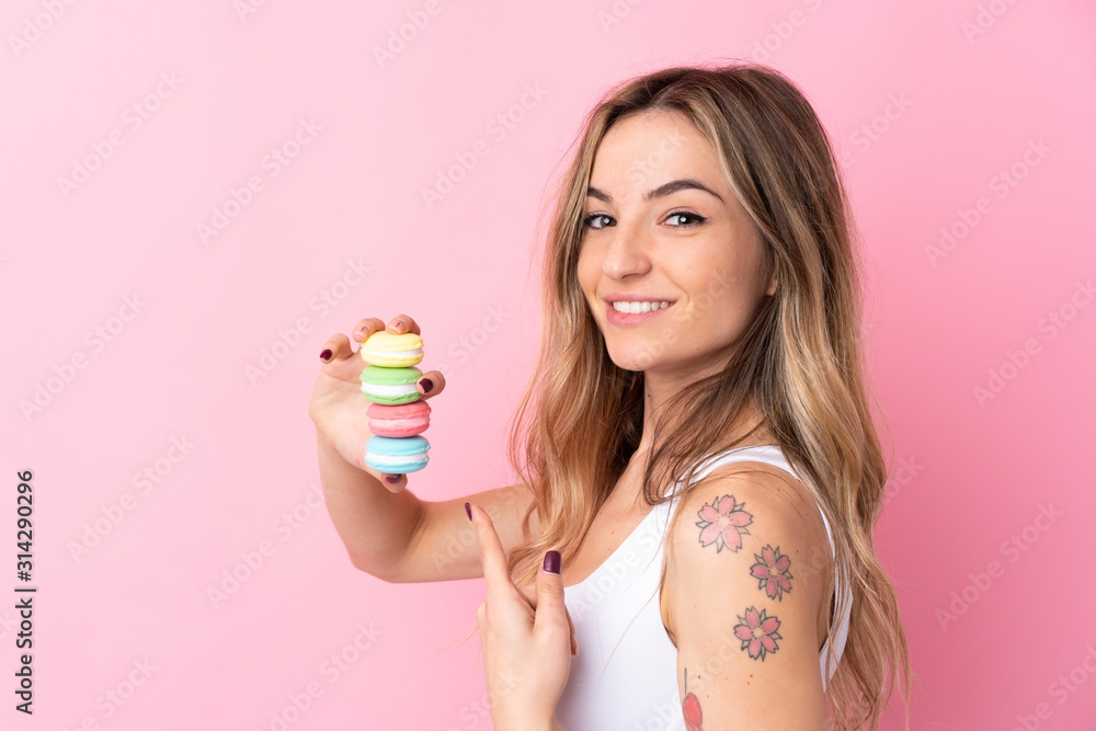 Young woman with macarons over isolated pink background and pointing it Young woman with macarons over isolated pink background and pointing it
