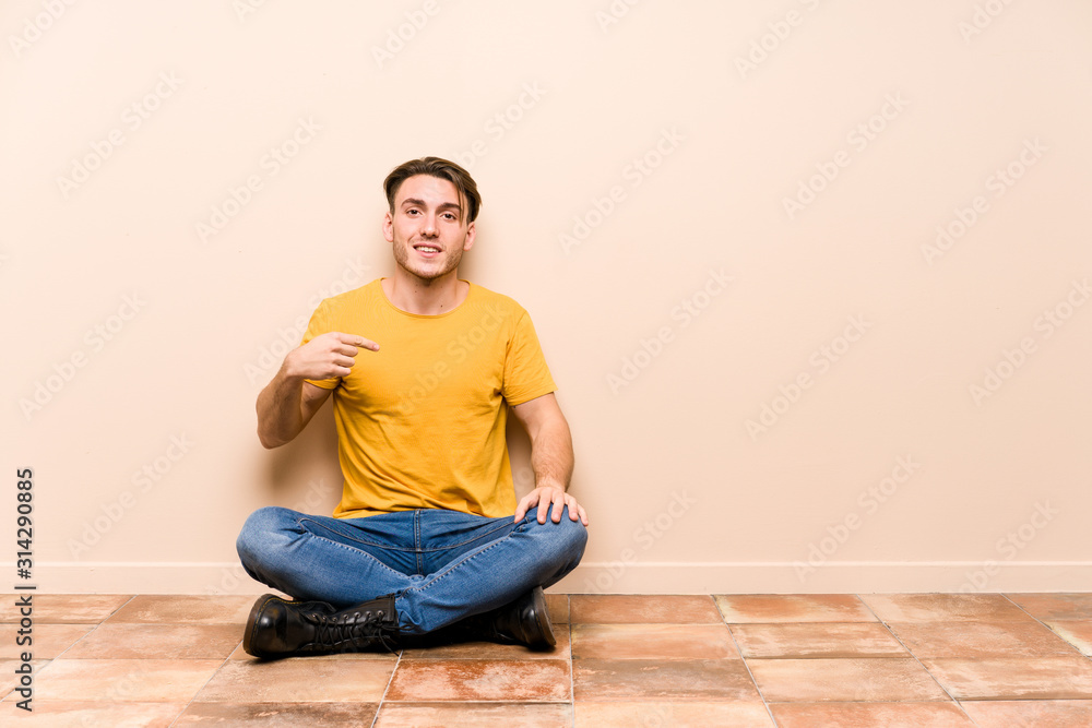 Young caucasian man sitting on the floor isolated person pointing by hand to a shirt copy space, proud and confident Young caucasian man sitting on the floor isolated person pointing by hand to a shirt copy space, proud and confident