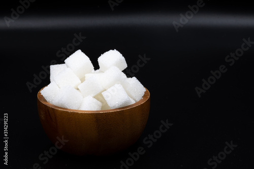 White sugar cube in wooden cup under black background.